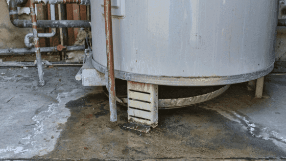 A close-up photograph showing a boiler with visible water damage and a puddle on the floor, indicating a boiler leaking problem. Keyword: boiler leaking.